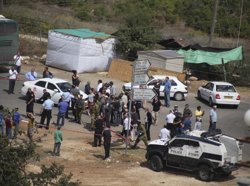 Israeli security forces and civilians stand at the scene of a stabbing attack outside the Jewish settlement of Kiryat Arba in the West Bank Friday Oct. 9 2015