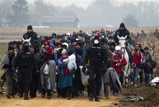 Escorted by police migrants move through fields after crossing from Croatia in Rigonce Slovenia Tuesday Oct. 27 2015. The European Union is lashing member countries for dragging their feet on providing funds and experts to help manage Europe's