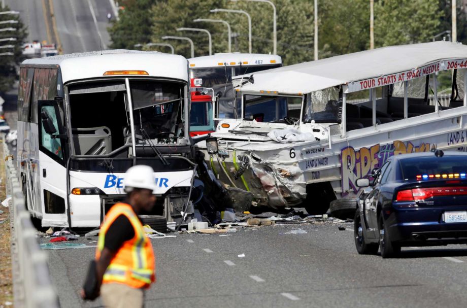 An emergency official stands near a charter bus left and a'Ride the Ducks amphibious tour bus following a fatal crash that killed five people Thursday Sept. 24 2015 in Seattle. The duck boat did not have an axle repair that was recommended for at