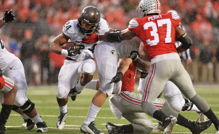 COLUMBUS OH- NOVEMBER 21 Gerald Holmes #24 of the Michigan State Spartans slices through the line for a gain in the second quarter as Joshua Perry #37 of the Ohio State Buckeyes attempts the tackle at Ohio Stadium