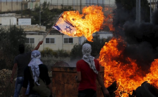 A Palestinian protester burns an Israeli flag during clashes with Israeli troops near the West Bank city of Ramallah on Oct. 30