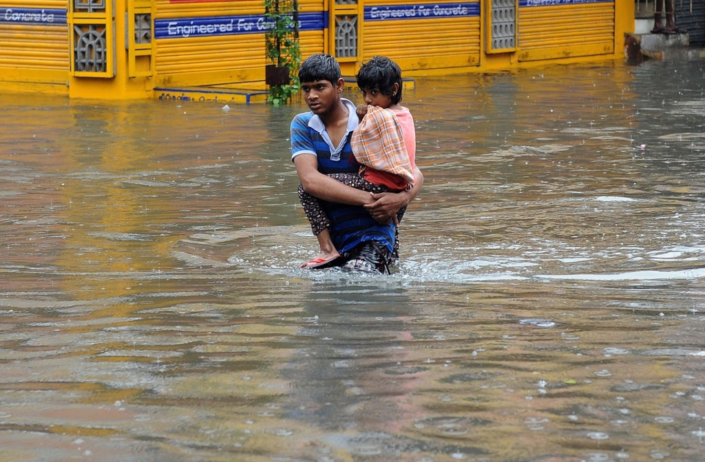 A boy carrying a kid walking in a water logged street in residential area flooded following heavy rains in Chennai India