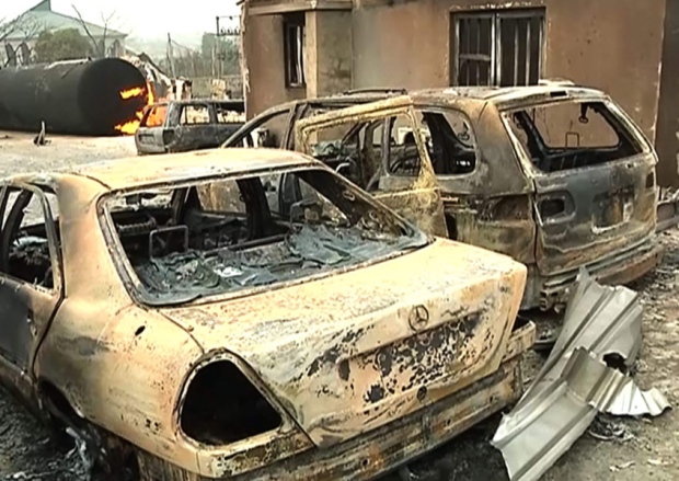 A burning cistern and burnt cars in the aftermath of a blast at an industrial gas plant in Nnewi southeastern Nigeria