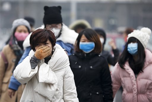 A woman uses her hand to cover her face from pollutants as people walk along a street on a polluted day in Beijing Tuesday Dec. 8 2015. Schools closed and rush-hour roads were much quieter than normal as Beijings first-ever red alert for smog took