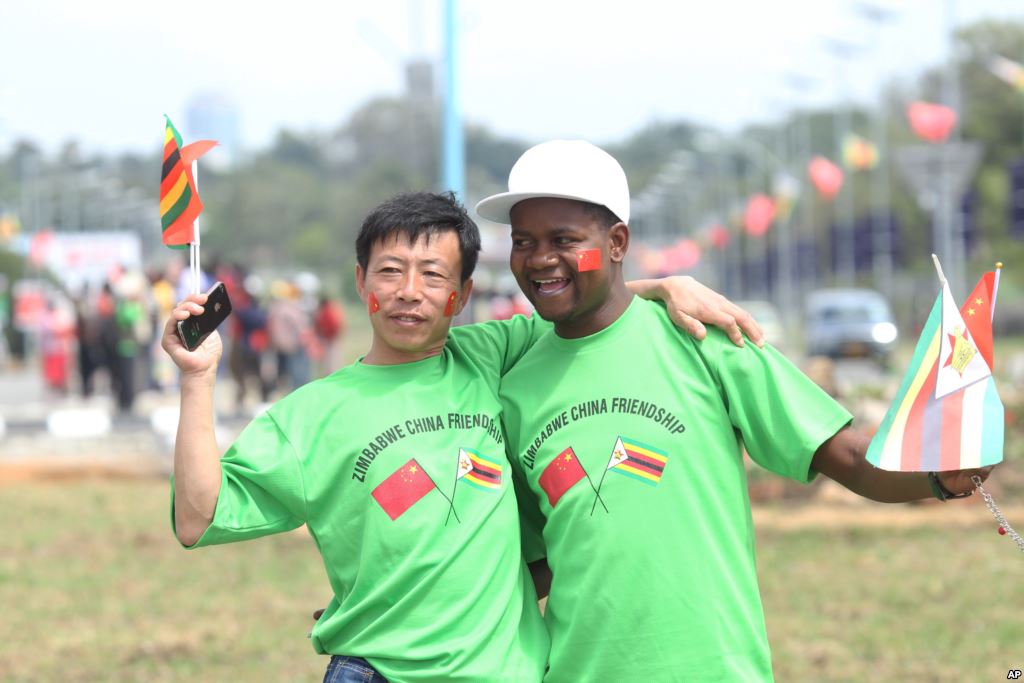 An unidentfied Chinese national and a Zimbabwean man hug while welcoming Chinese President Xi Jinping upon his arrival in Harare Zimbabwe Tuesday Dec. 1. 2015