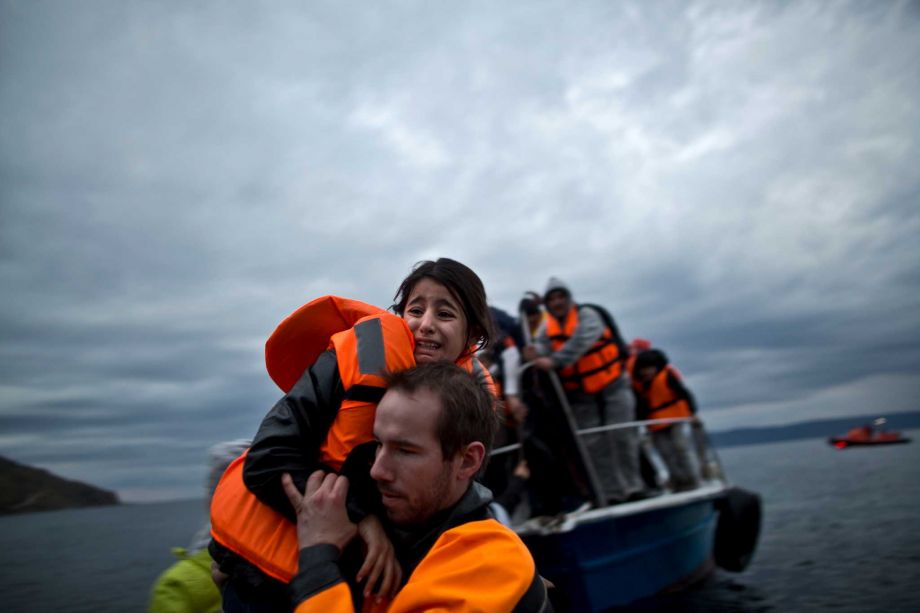 A young refugee girl is carried by a volunteer off a vessel to the shore shortly after arriving with her family from the Turkish coast to the northeastern Greek island of Lesbos Thursday Dec. 3 2015. The European Union's police agency says 23 suspects