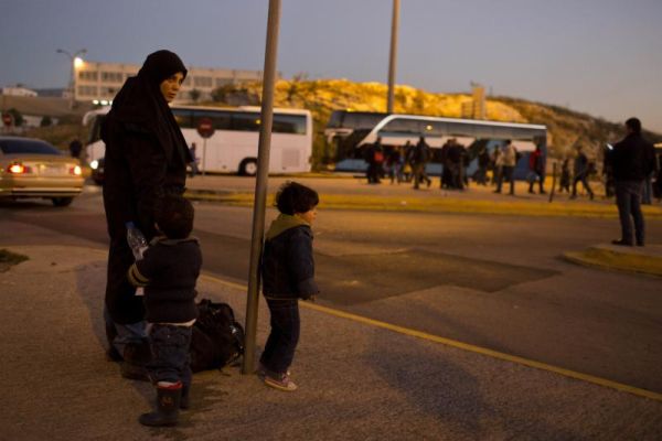 A Syrian woman with her children wait for