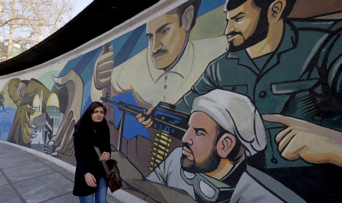 An Iranian woman walks past a revolutionary mural in Tehran Iran