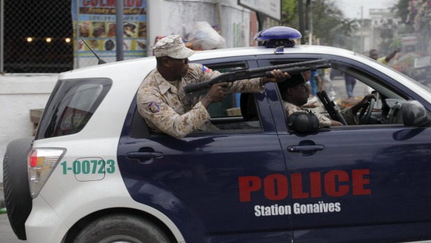 A National Police officer uses a shotgun to disperse protesters during a demonstration against the electoral process in Port-au-Prince