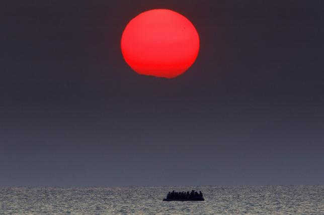 A red sun is seen over a dinghy overcrowded with Syrian refugees drifting in the Aegean sea between Turkey and Greece after its motor broke down off the Greek island of Kos