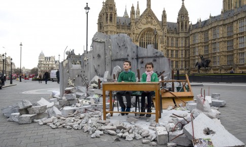 Two children whose school was bombed in Aleppo pose in a mock destroyed classroom — set up by the charity Save the Children — outside the Houses of Parliament in London on Wednesday one day before a donor conference aiming to raise money for victims