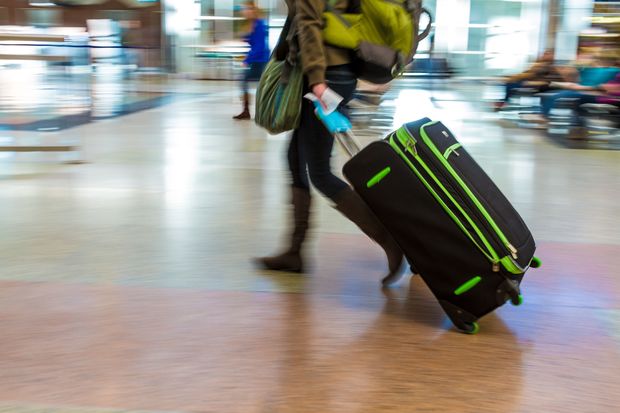 A woman with a backpack pulls a suitcase through an airport