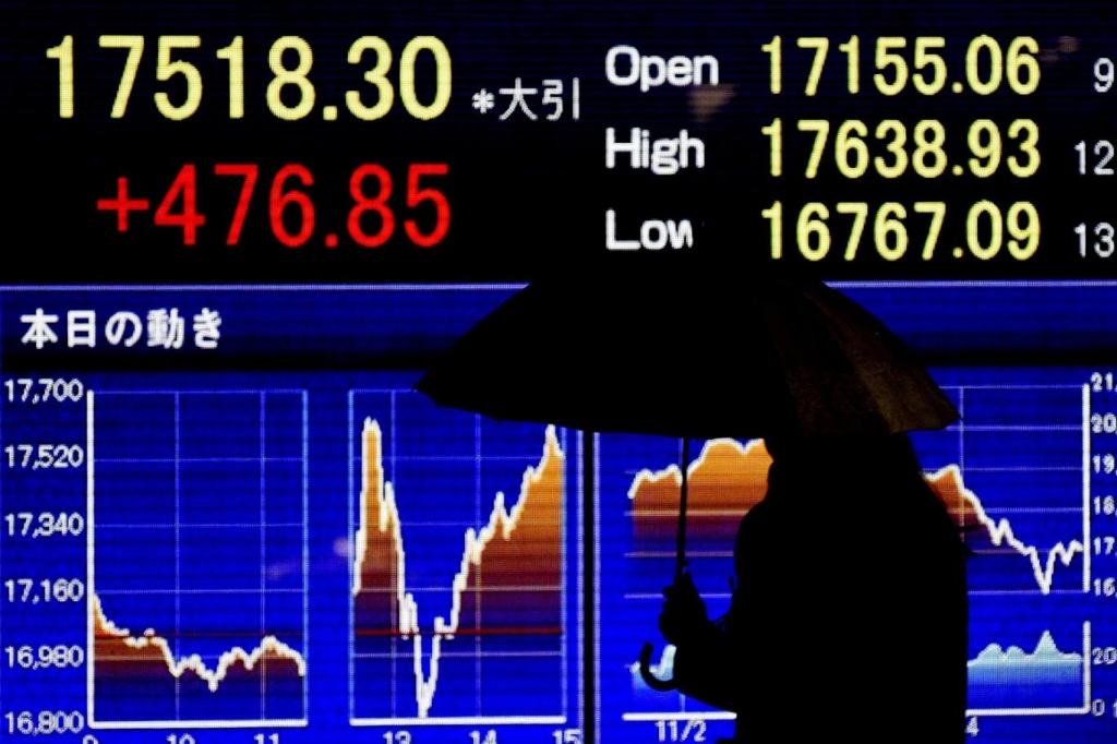 A pedestrian walks past a stock market indicator board in Tokyo