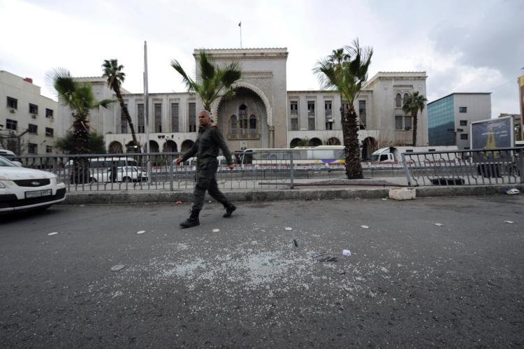 A Syrian security official walks near broken glass after a suicide blast at the Palace of Justice in Damascus Syria