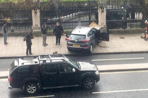 People stand near a crashed car on Bridge Street near the Houses of Parliament in London which was under terrorist attack on Wednesday