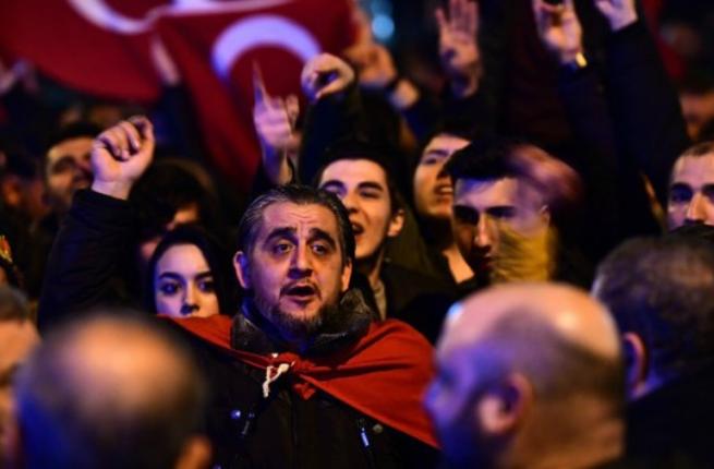 People gesture and wave flags as Turkish residents of the Netherlands gather for a protest outside Turkey's consulate in Rotterdam