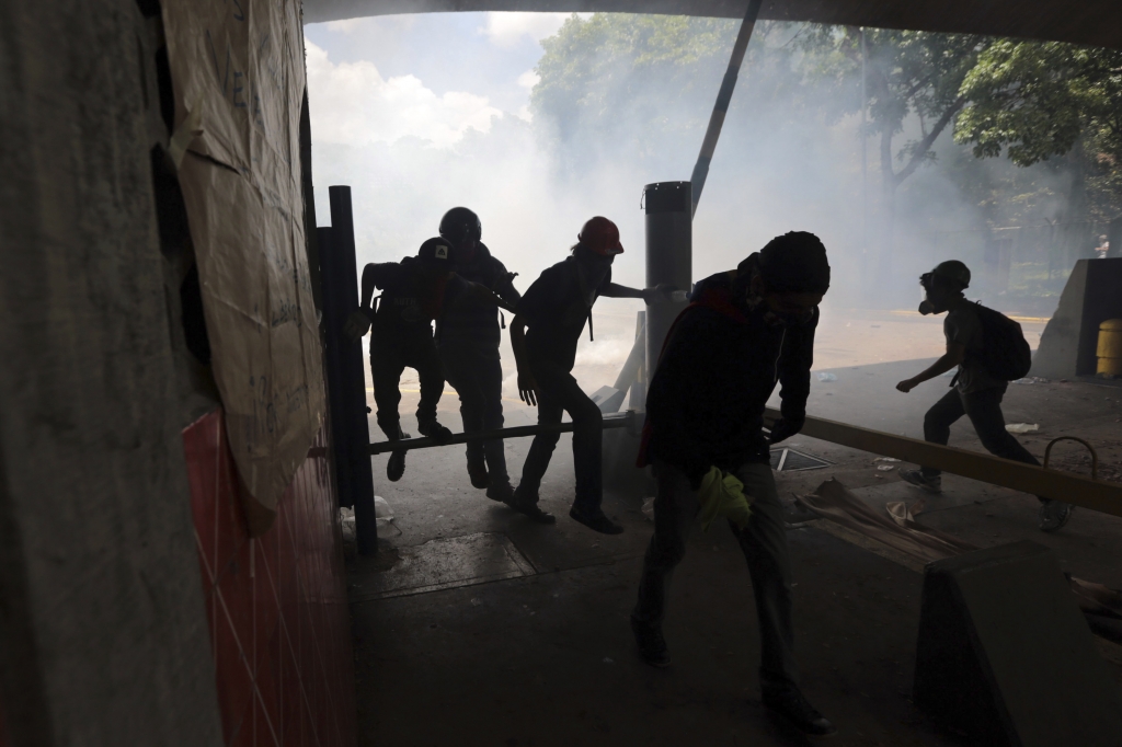 Students run from tear gas fired by National Police outside the Central University of Venezuela in Caracas Thursday