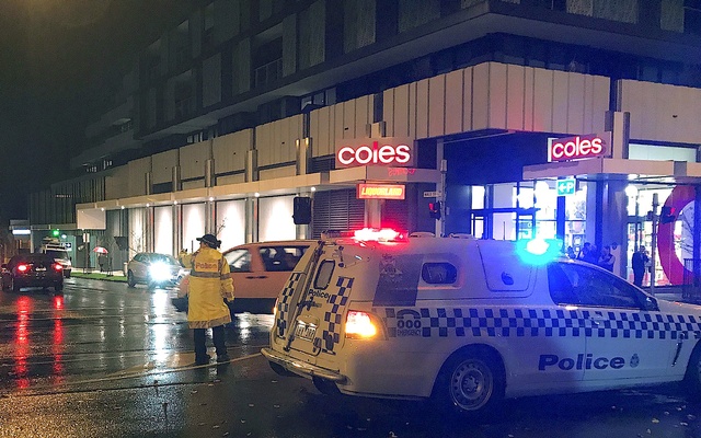 Police officer directs traffic near emergency services vehicles near the site of where a gunman was shot dead after holding a woman hostage in Melbourne Australia