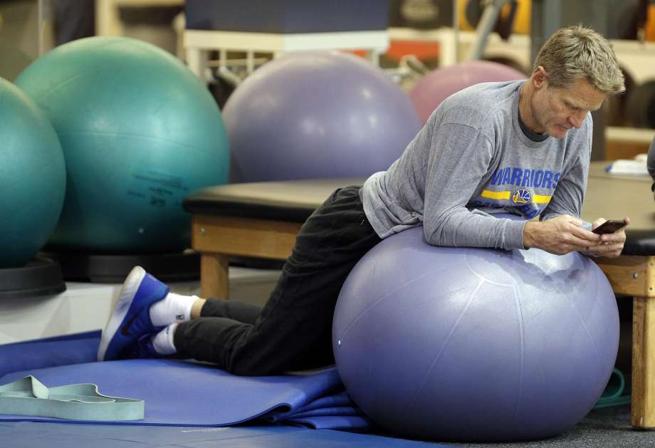 Warriors Head Coach Steve Kerr checks his phone as he watches players during practice at the Warriors headquarters in Oakland Calif. on Tuesday