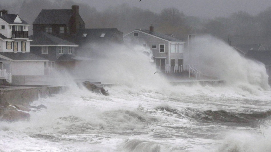 Waves splash against a seawall and onto houses along the Atlantic coast in Scituate Mass