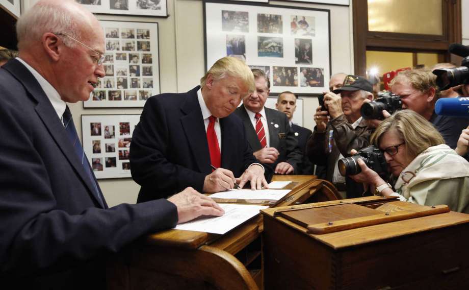 New Hampshire Secretary of State Bill Gardner watches left as Republican presidential candidate Donald Trump fills out his papers to be on the nation's earliest presidential primary ballot at The Secretary of State's