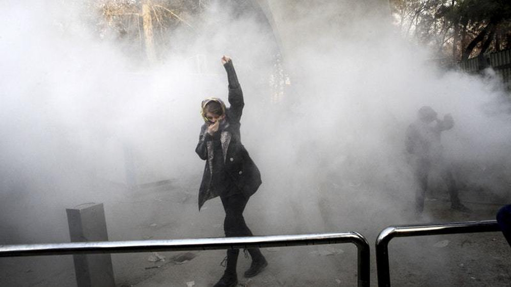 A university student attends a protest inside Tehran University while a smoke grenade is thrown by anti-riot Iranian police in Tehran Iran