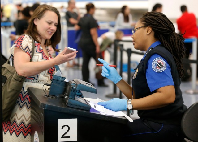 A TSA officer looks on as a traveler scans her boarding pass on her phone Tuesday