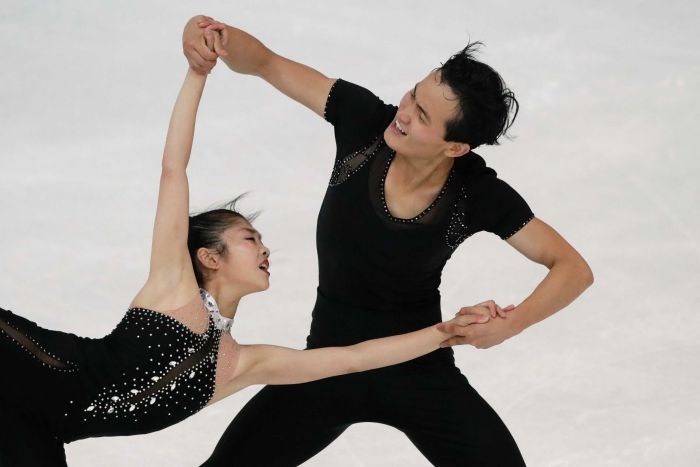 Male figure skater smiles as he spins his female partner