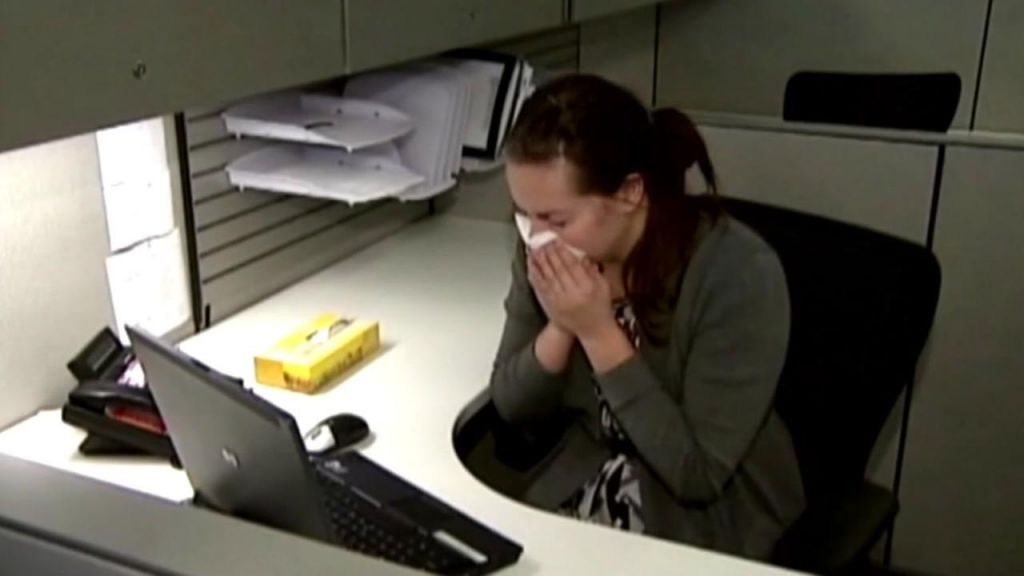 A woman sneezes into a tissue at her desk in this undated file