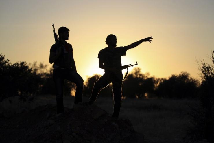 Free Syrian Army fighters are silhouetted as they stand on one of the front lines of Wadi Al Daif camp in the southern Idlib countryside