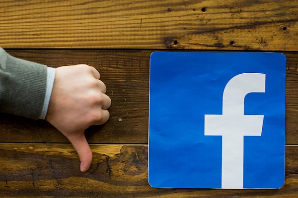 Person showing a thumbs down sign next to the Facebook logo