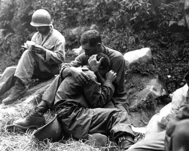 An American soldier comforts a fellow infantryman whose close friend has been killed in action Haktong-ni area Korea August 1950. A corpsman fills out casualty tags in the background. US Army