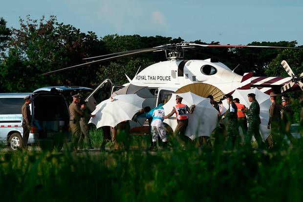 Police and military personnel use umbrellas to shield a rescued boy beng transferred on a stretcher from a helicopter to an ambulance after he emerged from the Tham Luang cave