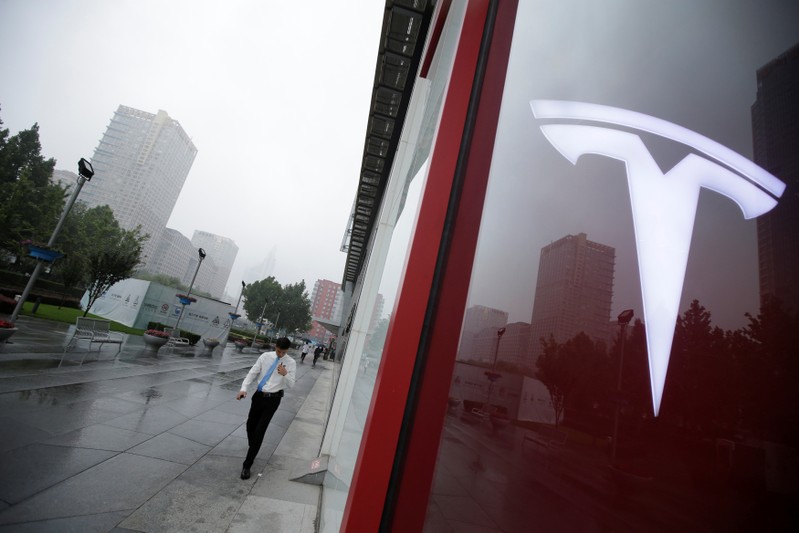 A man walks near a logo of Tesla outside its China headquarters in Beijing