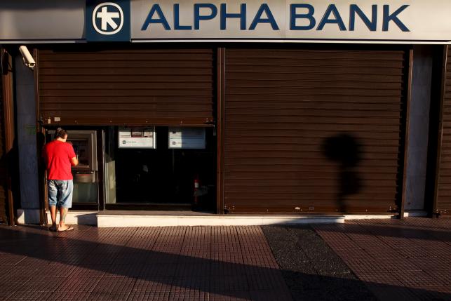 A man withdraws money at an Alpha Bank branch ATM in central Athens Greece