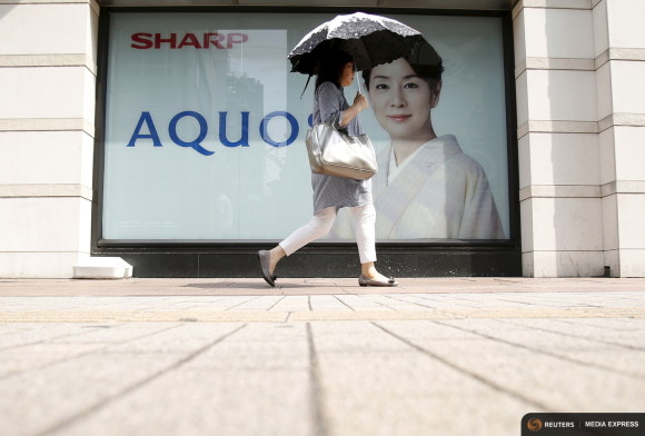 A woman holding her umbrella walks past an advertisement poster for Sharp Corp's Aquos outside an electronics shop in Tokyo Japan