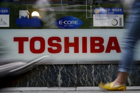 Pedestrians walk past a logo of Toshiba Corp outside an electronics retailer in Tokyo Japan