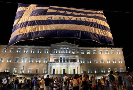 Anti-austerity protesters lift a Greek flag in front of the Greek Parliament in Athens