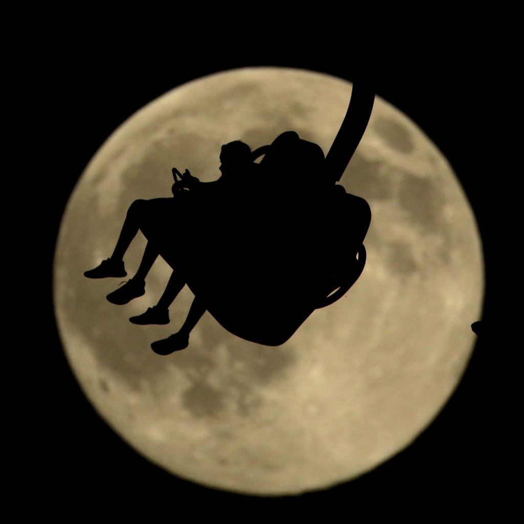 People are silhouetted against a nearly full moon as they ride an attraction at Worlds of Fun amusement park Thursday in Kansas City Mo. July 31 marks the second full moon of the month a rare occurrence that has come to be known as a'blue moon