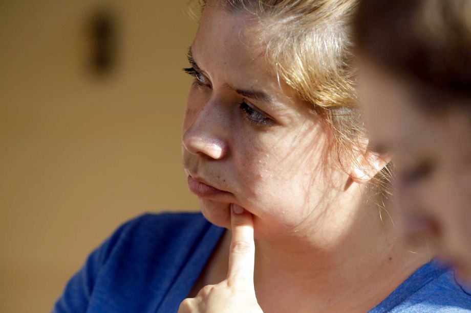 Dalila Mercado watches as officials continue to work the scene of a multiple shooting in her neighborhood Sunday Aug. 9 2015 in Houston. Eight people including five children and three adults were found dead inside a Houston-area home following the