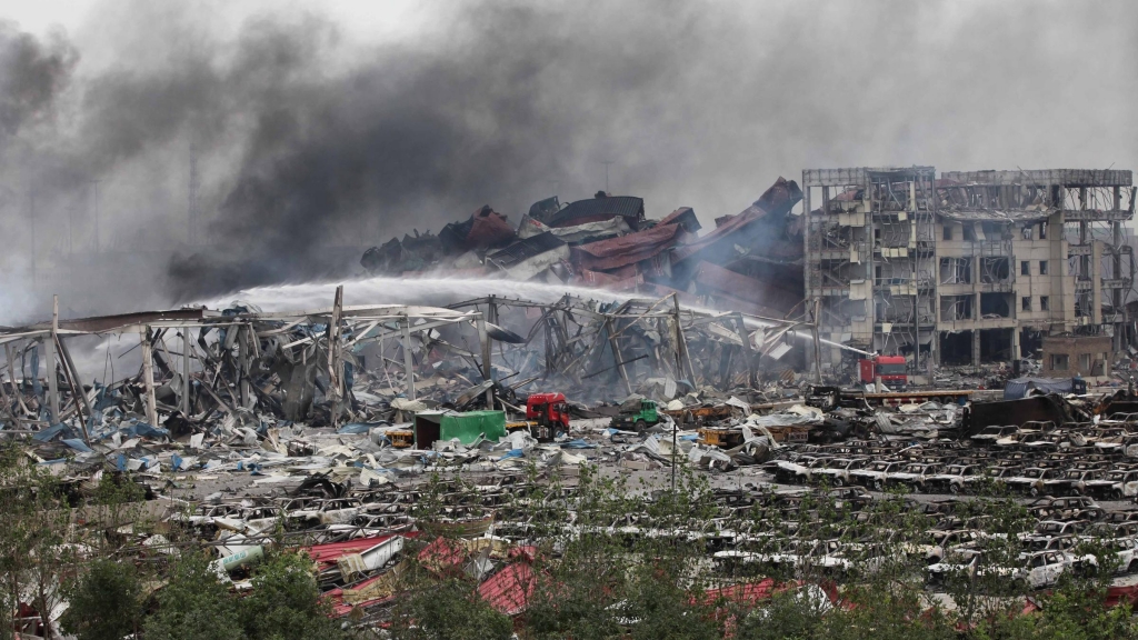 Firefighters work at the warehouse explosion site in Tianjin north China Friday. Scorched cars are in the foreground toppled shipping containers are in the background