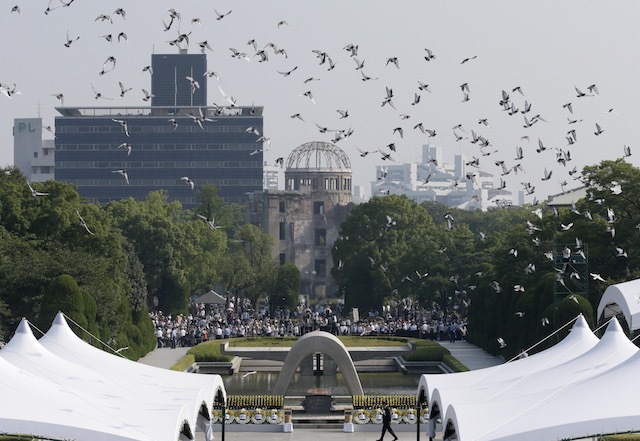 Doves fly over a cenotaph and the Atomic Bomb Dome during the peace memorial ceremony marking the 70th anniversary of the atomic bombing at Hiroshima Peace park