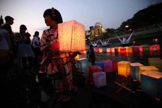 A girl wearing yukata or summer kimono prepares to release a paper lantern to the Motoyasu River where hundreds of thousands of atomic bombing victims died with the backdrop of the Atomic Bomb Dome in Hiroshima western Japan Thursday Aug. 6 2015. Japan