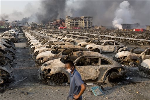 13 2015 a man walks past the charred remains of new cars at a parking lot near the site of an explosion at a warehouse in northeastern China's Tianjin municipality. Rescuers have pulled a survivor from an industrial