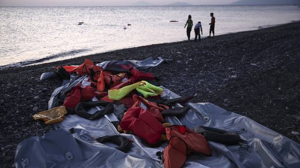 Life vests left behind by migrants on left a deflated dinghy as children play on the beach after crossing from Turkey to the Greek island of Kos