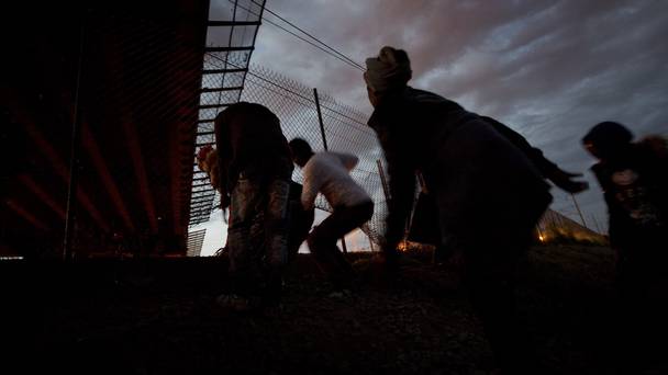 Migrants cross through a hole in the fence as they attempt to access the Channel Tunnel in Calais