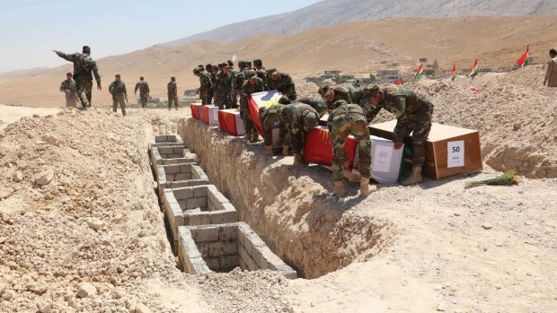 Kurdish peshmerga bury flag-draped coffins containing the remains of Yazidis who were killed by Islamic State militants