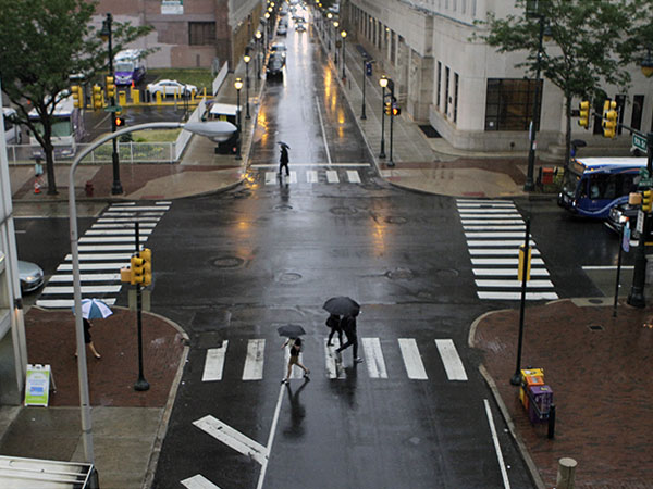 People with umbrellas walk across 9th Street at Market in Philadelphia