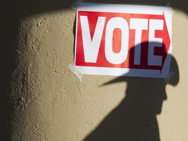 The shadow of a man wearing a cowboy hat falls on a pillar as he enters a polling place