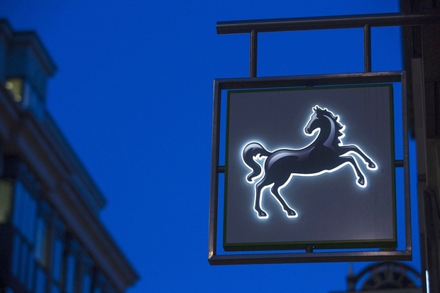 A logo is illuminated at dawn outside a Lloyds Bank branch in London